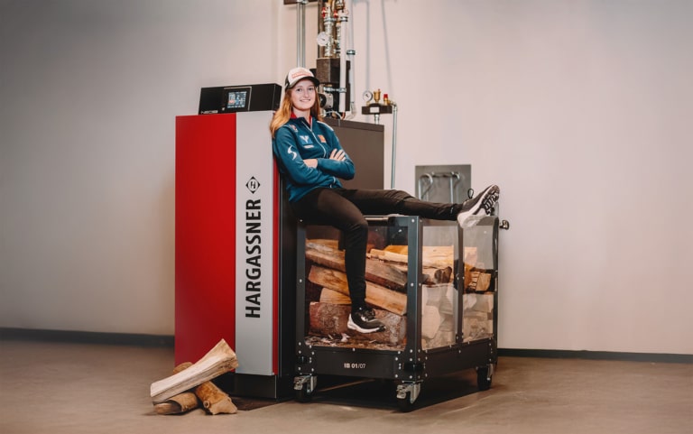 ÖSV athlete with logs next to a Hargassner boiler | Hargassner
