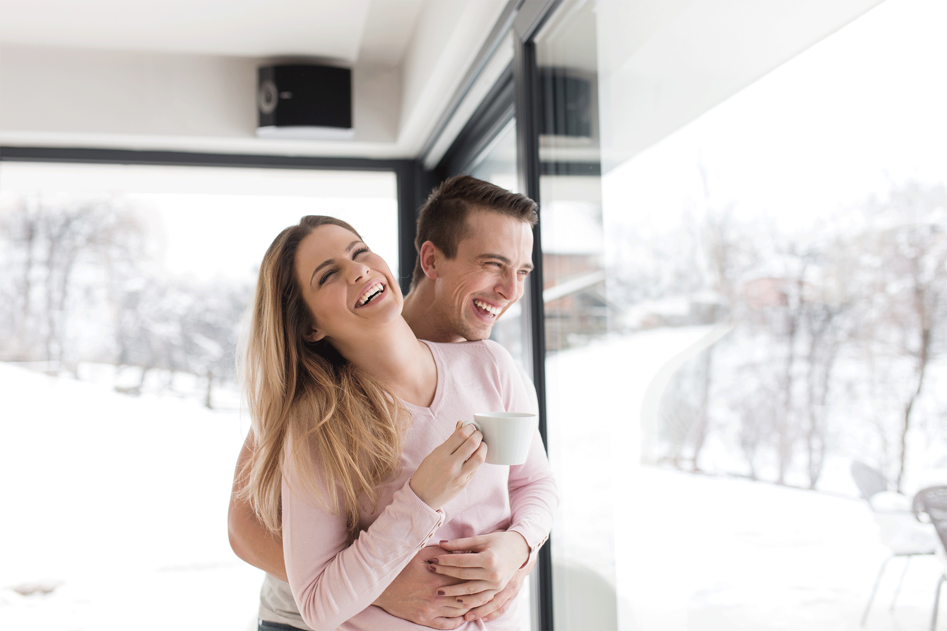 Paar steht am Fenster und freut sich - draußen ist Winter | Hargassner
