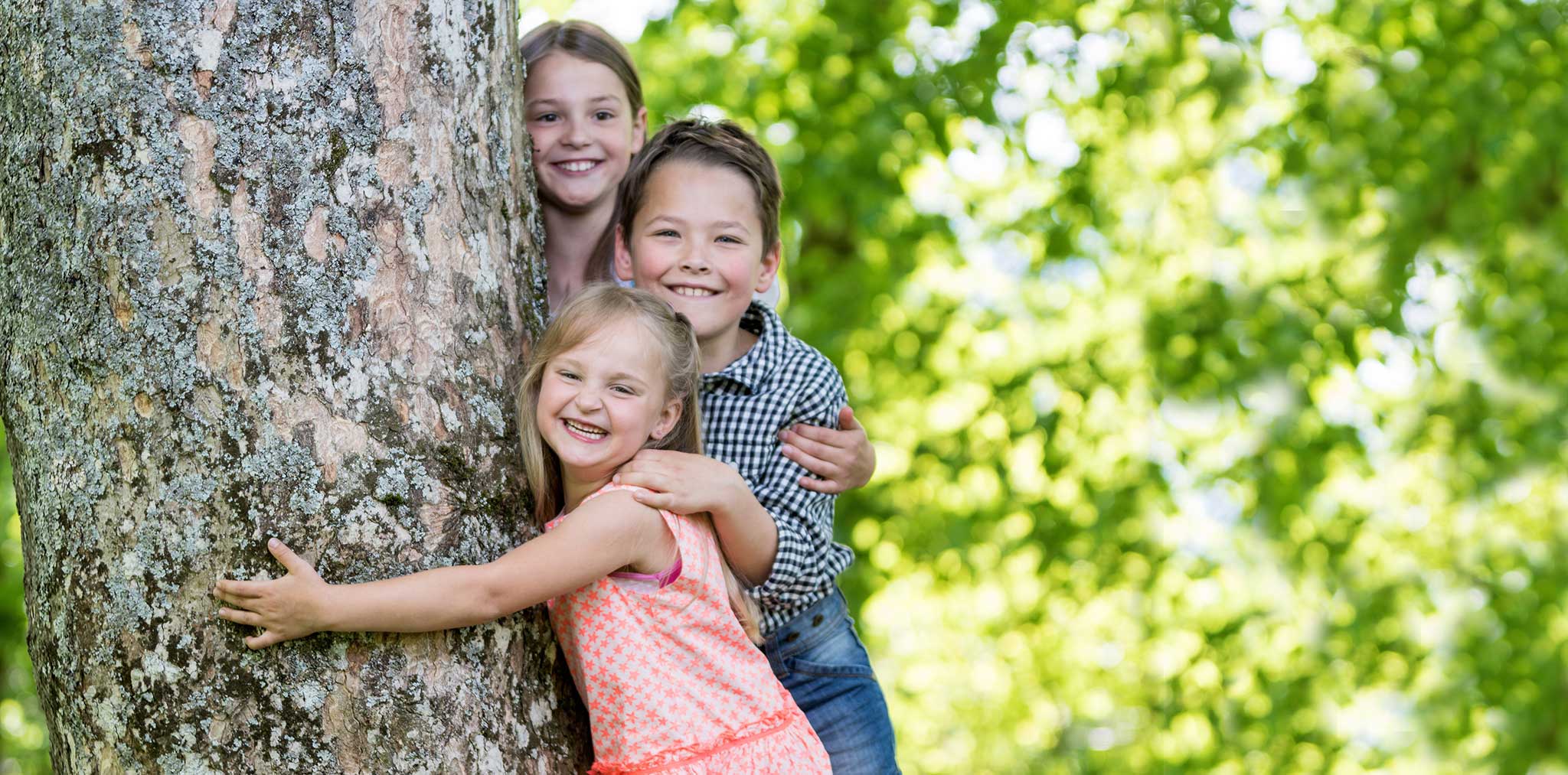 Kinder lachen und umarmen einen Baum