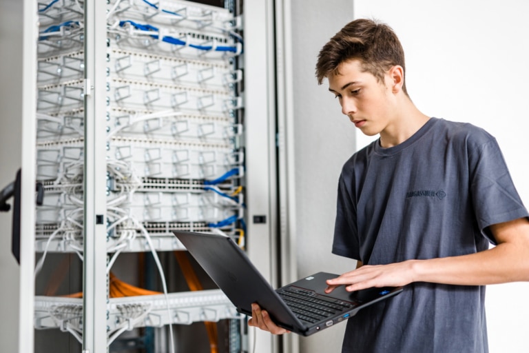IT-Lehrling mit grauem Shirt und Laptop vor dem Serverschrank | Hargassner