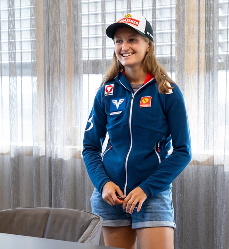 Julia Mühlbacher lächelt vor dem Fenster in Richtung Kamera