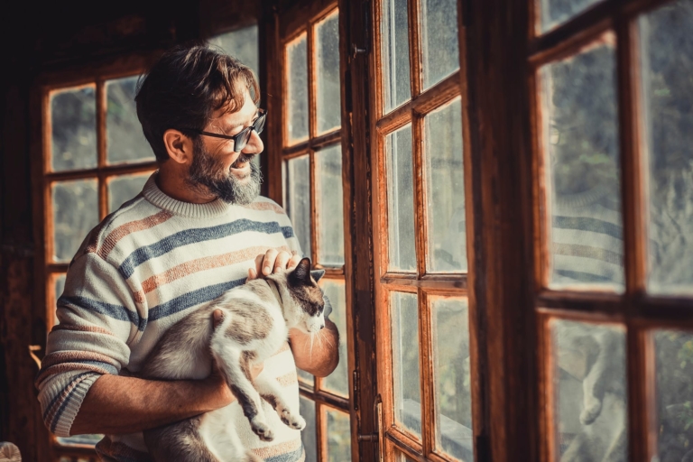 Homme souriant à la fenêtre avec un chat au bras | Hargassner