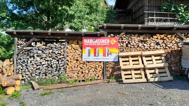 Brennholzstapel im Freien mit einem Werbebanner von Hargassner - Familie Frauenhuber Einfamilienhaus Stückholz | Referenz Hargassner