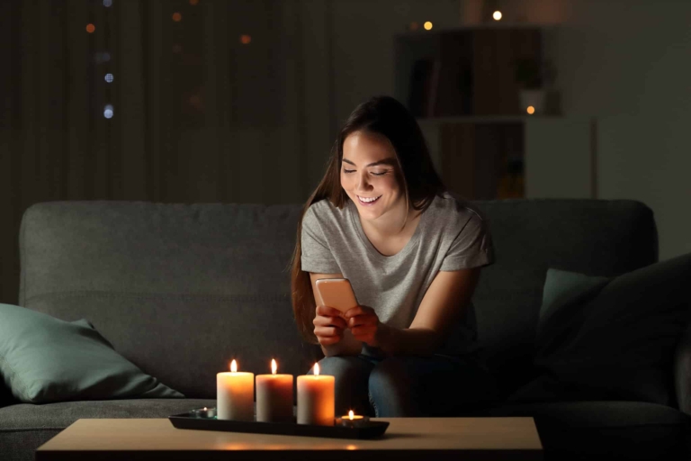 Femme assise sur un canapé dans l'obscurité à la lueur d'une bougie, souriante - Panne de courant - Blackout | Hargassner