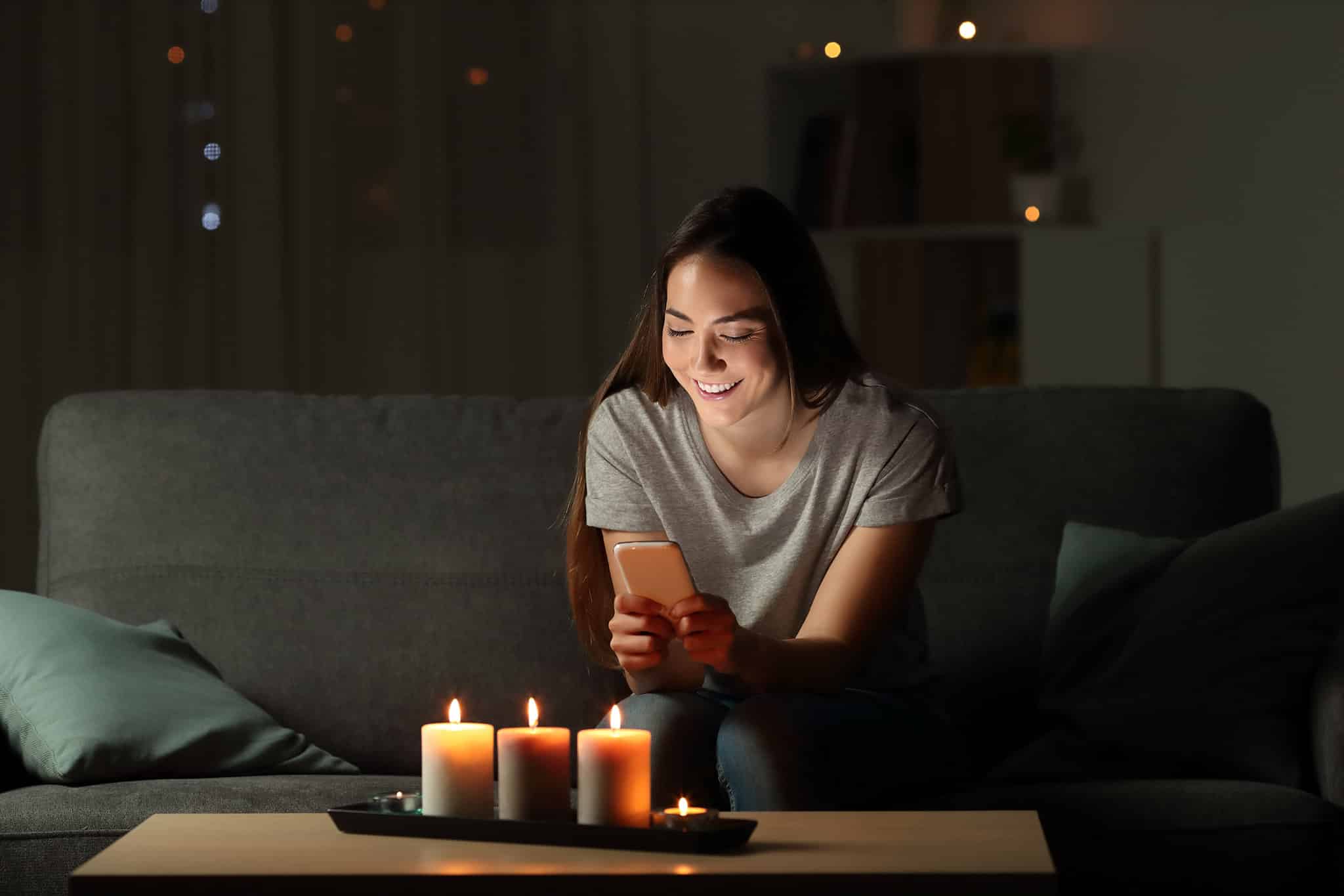 Frau sitzt im Dunkeln bei Kerzenschein lächelnd auf Sofa - Stromausfall - Blackout | Hargassner