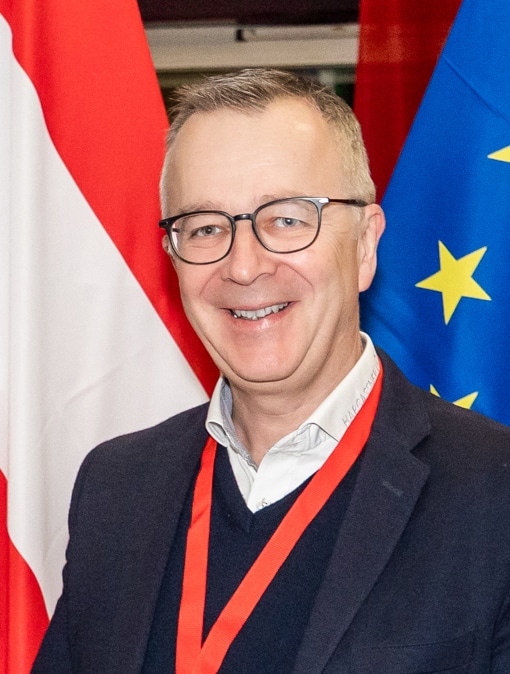 Verkaufsleiter Aichinger Wolfgang lachend vor einer Flagge von Österreich und der EU | Hargassner