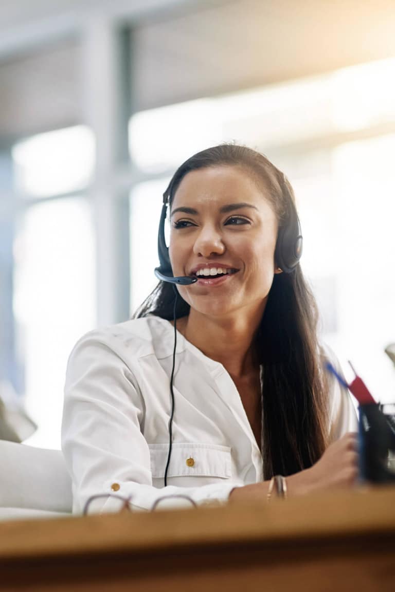 Frau am Schreibtisch telefoniert mit Headset und lächelt dabei