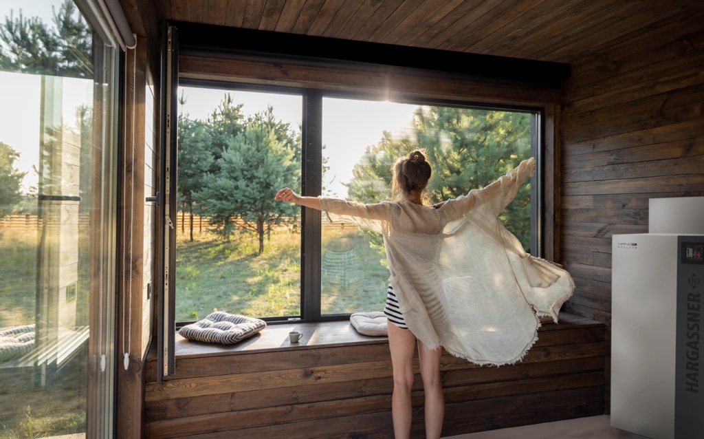 Femme debout devant la fenêtre, bras écartés, vue sur la nature