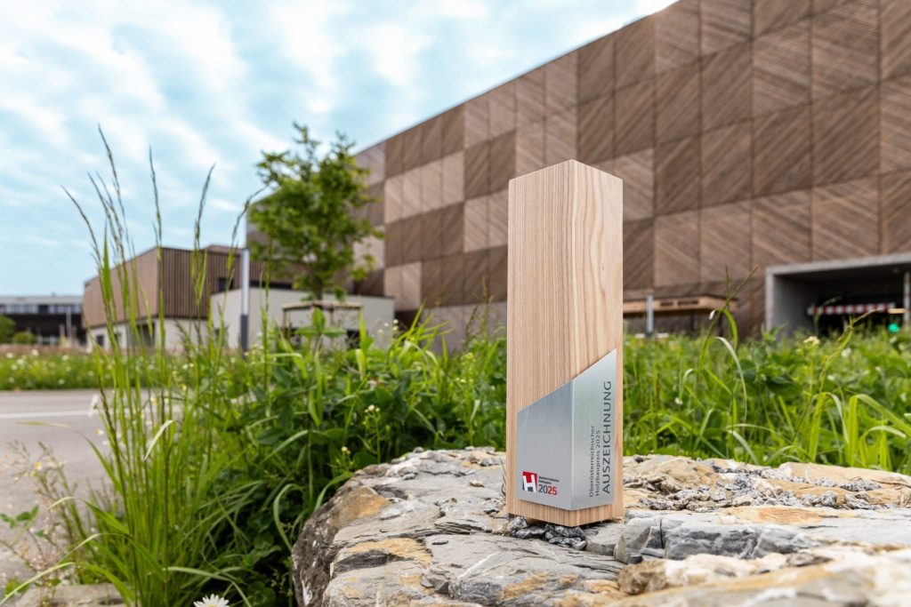 Die Trophäe für den oberösterreichischen Holzbaupreis 2025 vor der Einfahrt ins Hargassner-Holzparkhaus