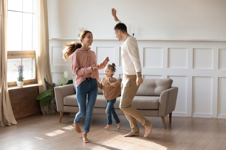Une famille danse pieds nus et en riant dans le salon