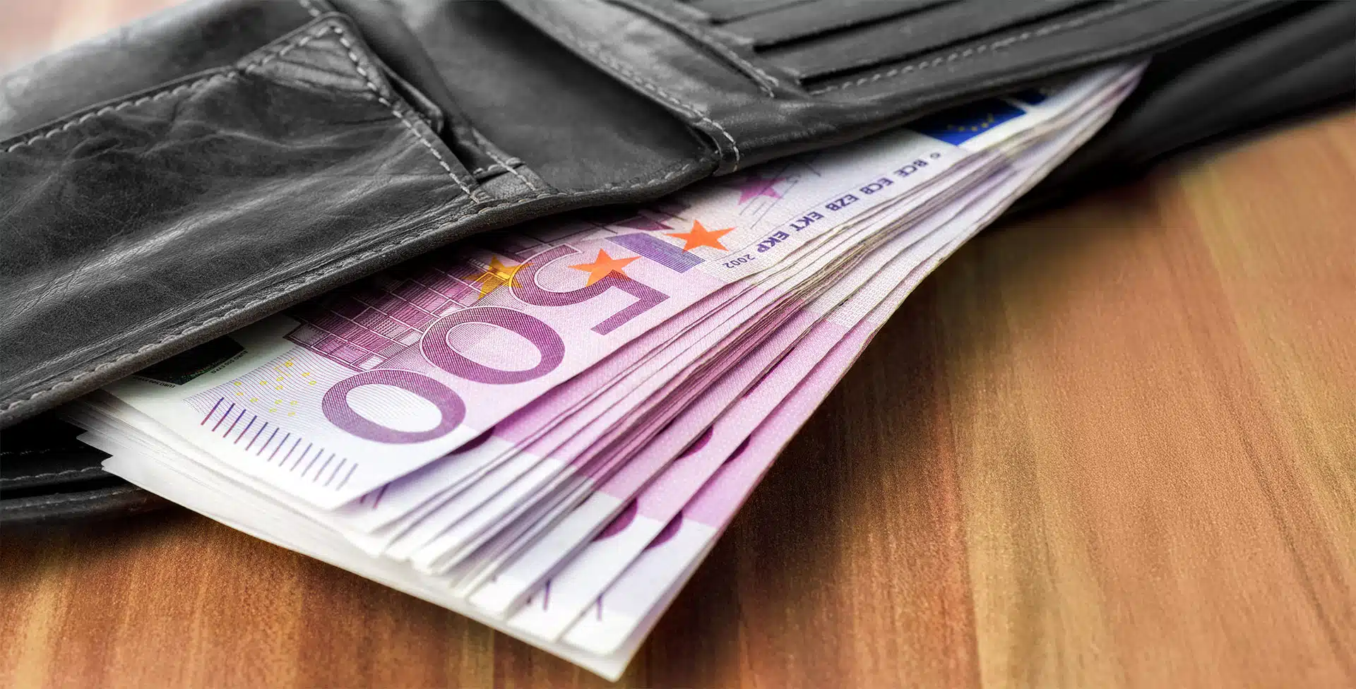 Geldtasche voll mit Fünfhunderteuro-Scheinen liegt offen auf einem Holztisch