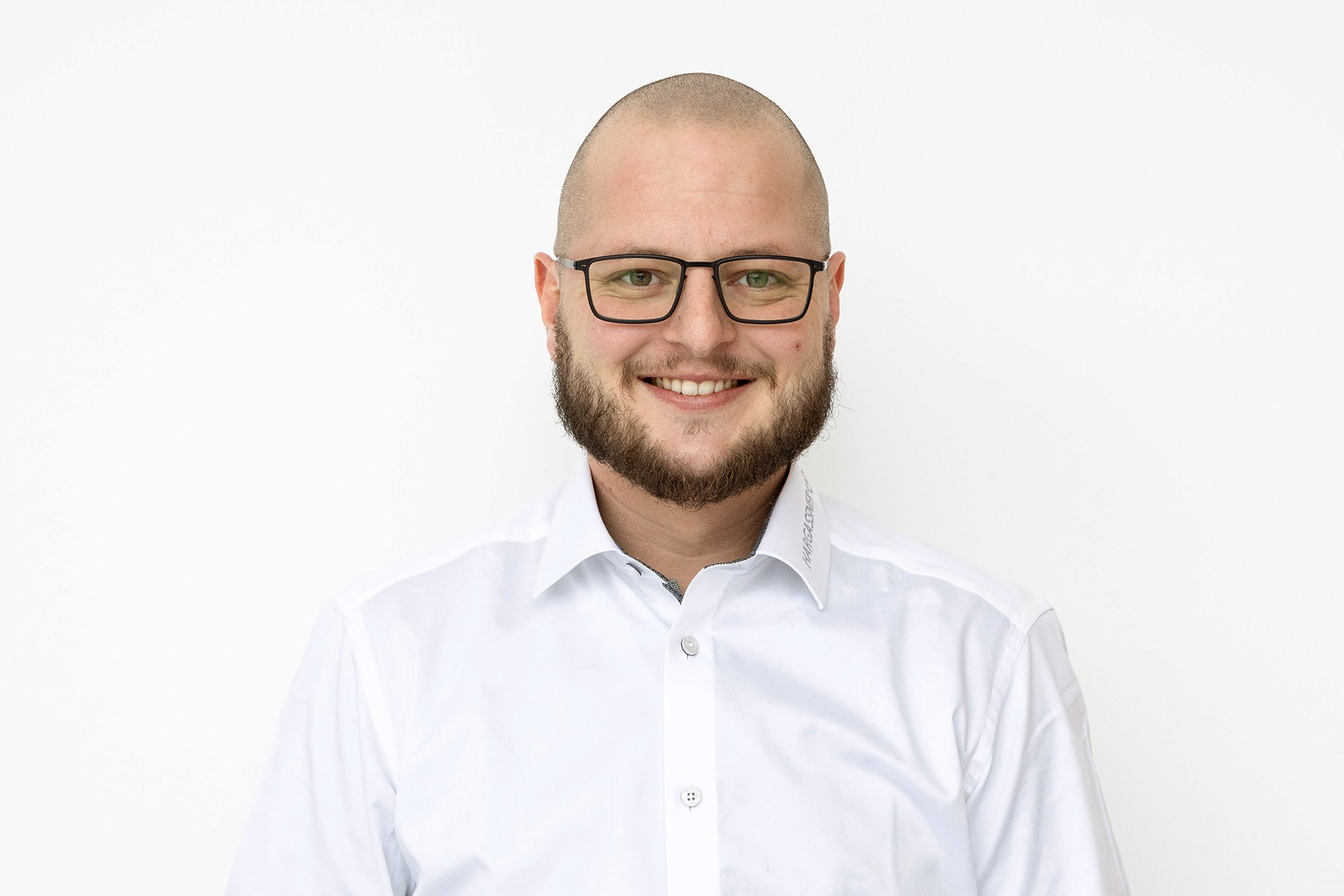 Profilbild Ansprechpartner Mathias Ruckerbauer mit Brille und weißem Hemd vor weißer Wand.